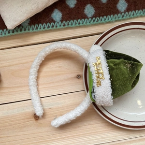 Detail of white plush Christmas headband with green velvet mini hat and gold Merry text