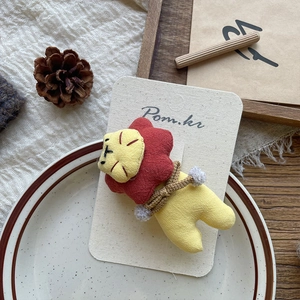 Detail of a handmade fabric lion hairpin with pompom on a decorative display card