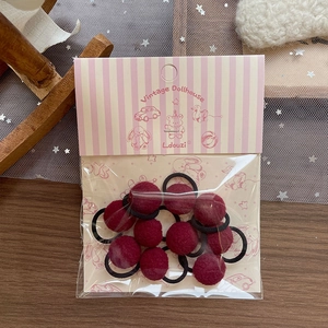 Detail of dark red plush ball hair ties in pink vintage packaging on wooden table