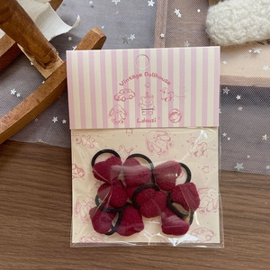 Close-up of deep red plush heart hair ties in vintage style packaging on a table
