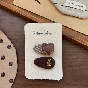 Detail of brown fabric hair clips with embroidered bear and gold metal bunny accents
