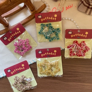 Five pairs of plush star hair clips in multiple colors on a textured cream tablecloth