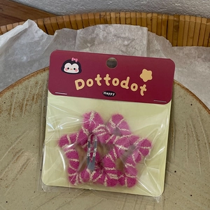 Detail of star-shaped hair clips in rosy pink plush texture on brand display card