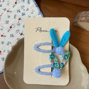 Detail of blue floral bunny ear hair clips for girls with soft plush pom pom accents