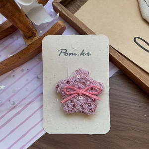 Détail d'une pince à cheveux étoile en tweed rose avec paillettes et nœud