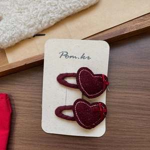 Detail view of two burgundy heart-shaped plush hair clips with white stitching and bows