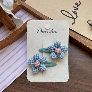 Detailed macro view of two sweet checkered floral hair clips on a cream display card