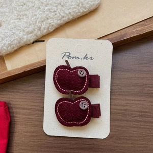 Detail of red apple-shaped fabric hair clips with pink stitching on white display card