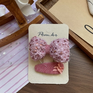 Détail du set de barrettes avec nœud rose à paillettes et tissu en tweed élégant