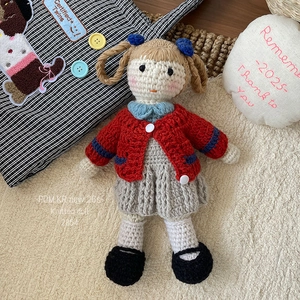 Detailed close-up of handmade knitted doll with brown braids and red cardigan sweater