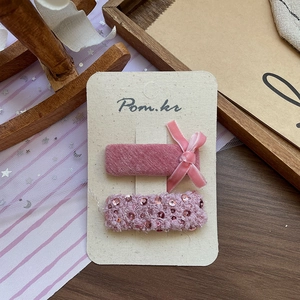 Gros plan sur la barrette à nœud rose en velours et épingles à paillettes sur emballage