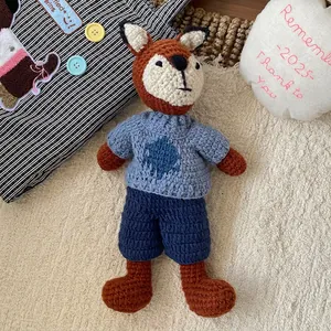 Detailed close-up of a handmade crochet fox doll wearing a blue knitted sweater on soft rug