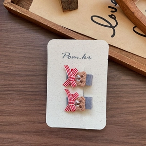 Detail of two handmade bear fabric hair clips with red plaid bows on display card