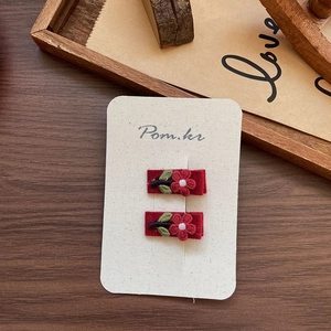 Detail of two handmade red floral embroidered hair clips on a white display card