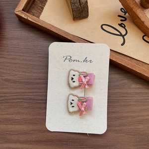 Detail shot of two embroidered cartoon bear hair clips on white cardstock with a pink bow