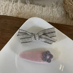 Détail de la pince à cheveux à nœud gris et clip fleur en velours rose sur plat