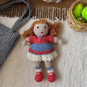 Detail of handcrafted crochet doll with curly hair wearing a striped dress on white carpet