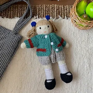Macro shot of handmade crochet doll in green cardigan on white textured carpet