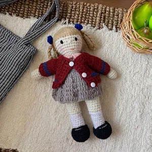 Detail of a handmade crochet doll with blonde pigtails in a red knit cardigan