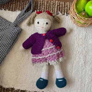 Detail of handmade crochet doll wearing a purple cardigan and pink dress on a soft rug