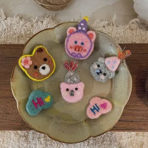 Handmade wool felt cartoon bear and cloud brooches displayed on a decorative ceramic plate