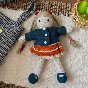 Detail showing handcrafted crochet doll with brown braids and blue cardigan outfit