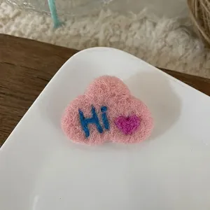 Detailed view of pink wool felt heart brooch with Hi embroidery and soft texture