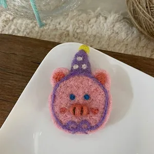 Detail of pink wool felt pig brooch with purple birthday hat on a white ceramic plate