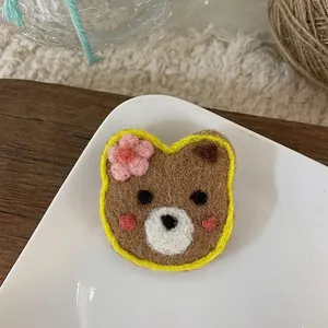 Macro shot of a handmade wool felt brown bear brooch with pink flower detail in a tray