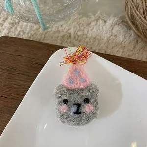 Detail of handmade wool felt grey bear brooch with pink party hat and tassels