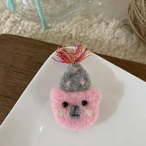 Close-up of handmade pink wool felt bear brooch with a grey hat and colorful tassels