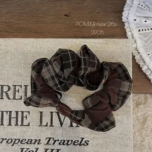Detailed view of a brown plaid scrunchie with a decorative resin bead on vintage book