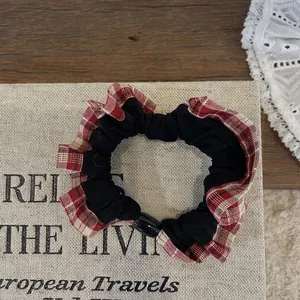 Detail of a large black scrunchie with red plaid ruffle trim on a decorative beige card