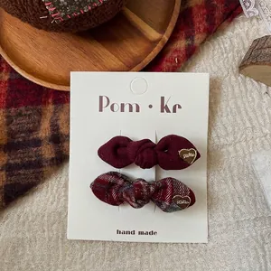 Detail of red plaid and wine red bow hair clips with gold heart charms on display card