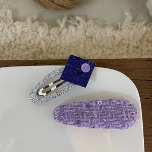 Close-up of purple fabric bow and blue sequin hair clip set on a white ceramic plate