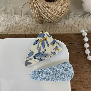 Close-up of blue floral fabric snap clip and woven hair clip on a white ceramic plate