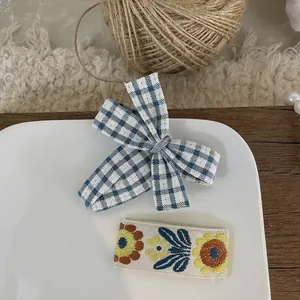 Close-up of blue gingham bow hair clip and sunflower embroidered snap barrette