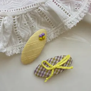 Détail d'une pince BB jaune perlée et d'un nœud à carreaux violets sur tissu dentelle