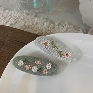 Nahaufnahme der Blumenstickerei auf ovalen Stoff-Haarspangen mit feinen Details