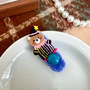 Dettaglio di un fermaglio per capelli in peluche viola con orsetto ricamato su un piatto
