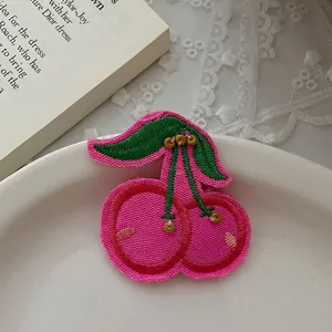 Détail de la broderie cerise pour pince à cheveux avec perles et feuilles vertes
