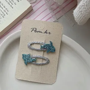 Detail of blue glitter dolphin hair clips with silver thread wrap on display card