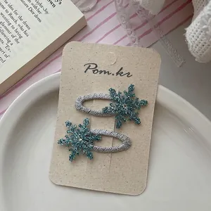 Close-up of blue glitter snowflake hair clips with diamond accents on a cream card