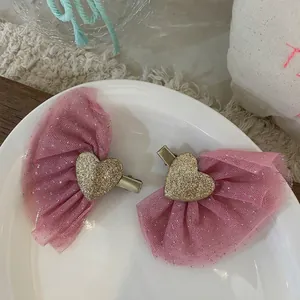 Detail view of pink mesh bow hair clips with gold glitter hearts on white ceramic plate