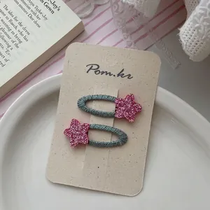 Detailed view of pink glitter star and teal woven hair clips on a cream display card