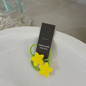 Détail d'élastiques à cheveux étoiles jaunes sur cordelette verte avec emballage de marque