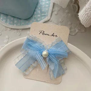 Détail d'une pince à cheveux nœud en organza bleu avec perle sur carte de présentation