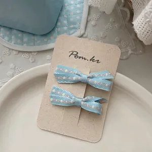 Détail des barrettes à nœud bleu avec bords brodés présentées sur une carte de support