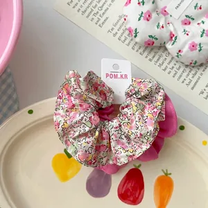 Vue détaillée d'une pince à cheveux en tissu floral avec base rose à volants sur carton