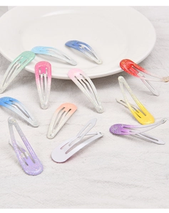 Detail of colorful gradient glitter teardrop hair clips scattered on a white ceramic plate